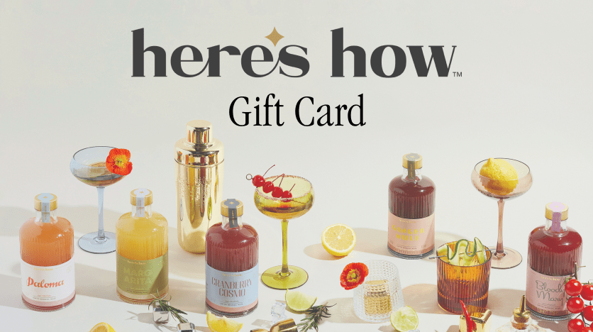 A Heres How Gift Card is displayed among cocktails and mixers in glassware and bottles, garnished with fruit and herbs, with a gold cocktail shaker in the background—the perfect gift for any occasion.