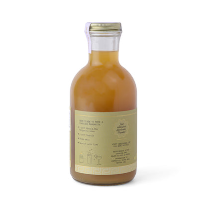 A clear glass bottle labeled Margarita with a gold label, filled with yellow-orange liquid and cocktail mixing instructions, set against a plain white background.