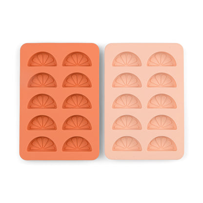 The Dotty Citrus Wedge Ice Trays, one orange and one light pink, each with six citrus wedge-shaped cavities, add a playful touch to your drinks by making fun ice cubes.