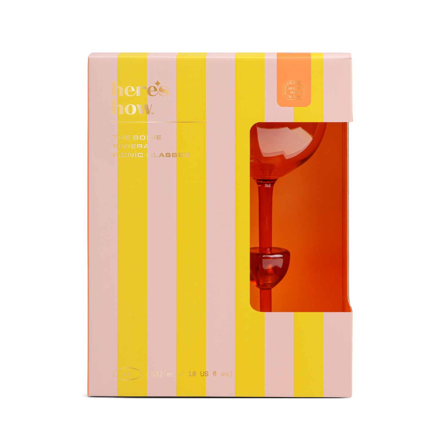 A boxed set of The Bodie Riviera Glass is partially visible through a window in pink and yellow striped packaging labeled heres how, perfect for picnics or outdoor enjoyment.