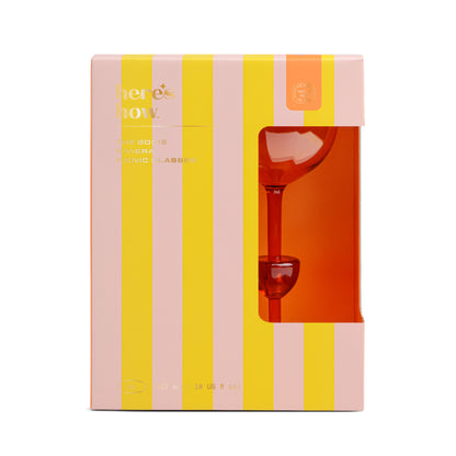 A boxed set of The Bodie Riviera Glass is partially visible through a window in pink and yellow striped packaging labeled heres how, perfect for picnics or outdoor enjoyment.