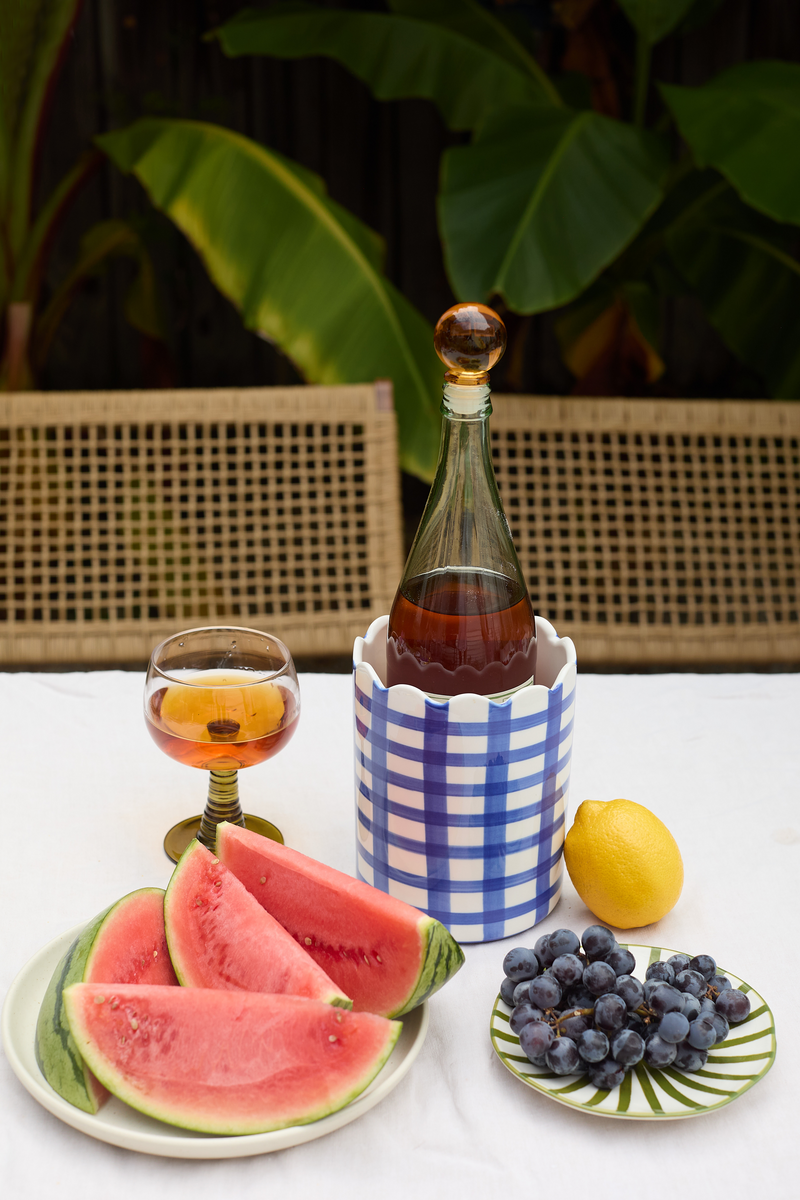 Fruit platter with watermelon, grapes, lemon, and a bottle of wine on a checkered coaster.