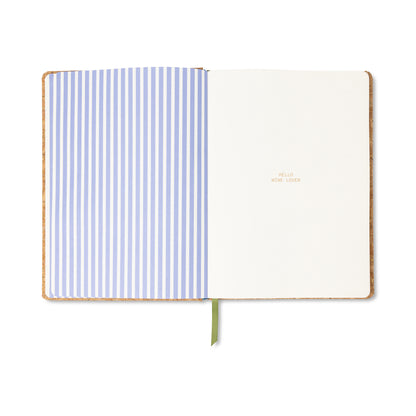 Open notebook showing left page with blue and white vertical stripes, and right blank page with small text reading HELLO WINE LOVER. Green ribbon bookmark is visible— the ideal Cork Wine Bottle Wine Journal for recording your tasting notes.
