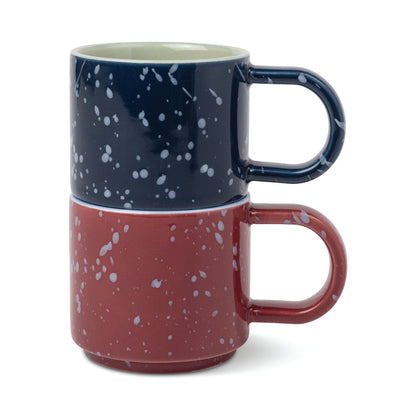 A navy blue espresso cup stacked on top of a burgundy espresso cup from The Simon Espresso Cups Set - Burgundy + Navy, both featuring a white speckled pattern.