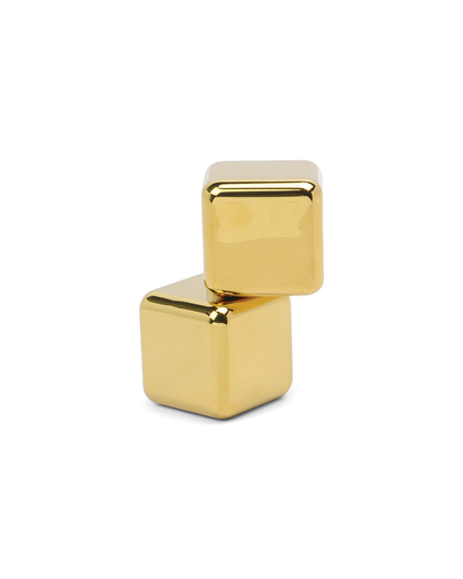 Two shiny gold The Jupiter cubes are stacked against a plain white background, serving as stainless-steel cocktail chillers that keep drinks cold without dilution.
