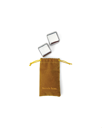 Two freezable stainless-steel cocktail chillers, The Jupiter, rest above a closed brown drawstring pouch labeled “here’s how,” set against a white background.