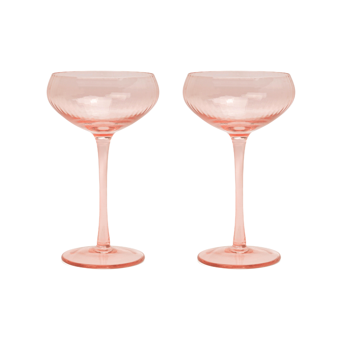 Two The Lou pink soda lime glass coupe champagne glasses stand side by side on a white background, perfect for serving your favorite craft cocktails.